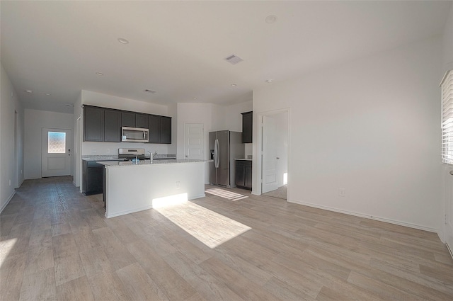 kitchen with light stone countertops, light hardwood / wood-style flooring, an island with sink, and stainless steel appliances