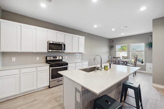 kitchen with appliances with stainless steel finishes, a breakfast bar, a kitchen island with sink, sink, and white cabinets