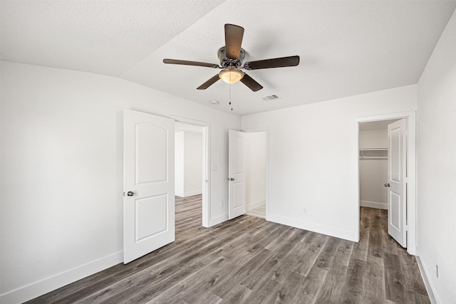 unfurnished bedroom featuring a walk in closet, a textured ceiling, ceiling fan, dark hardwood / wood-style floors, and a closet