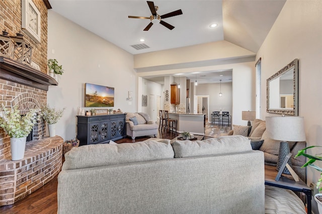 living room with ceiling fan, dark hardwood / wood-style floors, lofted ceiling, and a brick fireplace