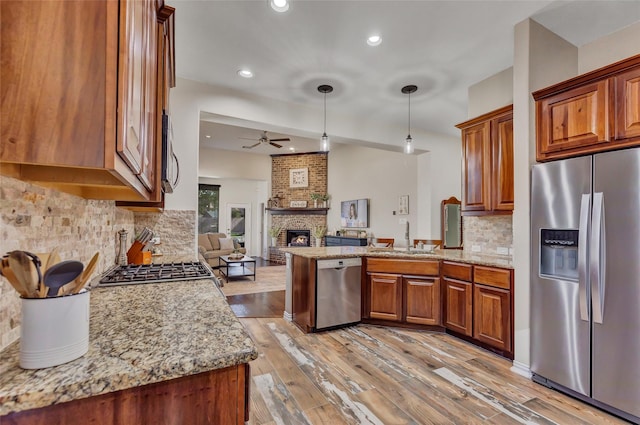 kitchen with a brick fireplace, tasteful backsplash, light stone counters, decorative light fixtures, and appliances with stainless steel finishes