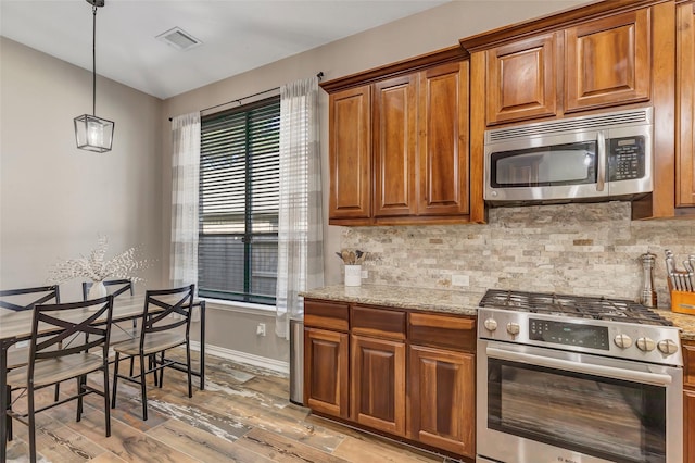 kitchen with backsplash, hanging light fixtures, light hardwood / wood-style flooring, light stone countertops, and stainless steel appliances