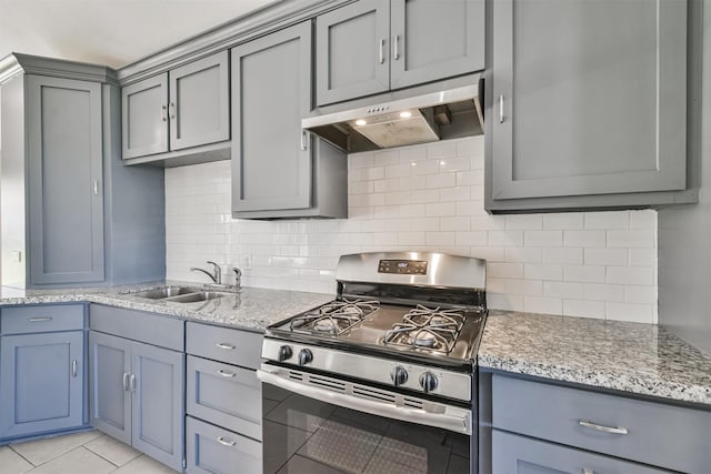 kitchen with decorative backsplash, light stone counters, sink, and gas range