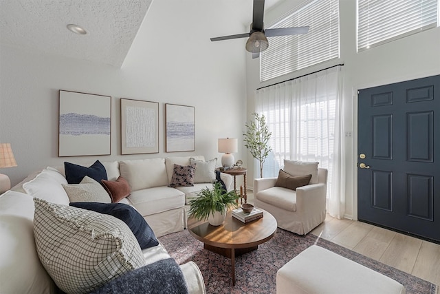 living room with ceiling fan, high vaulted ceiling, a textured ceiling, and light wood-type flooring