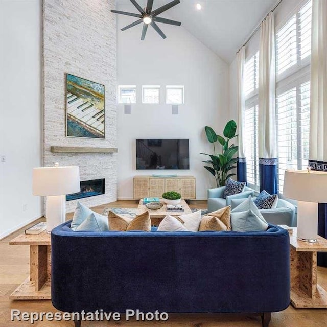 living room with ceiling fan, a fireplace, high vaulted ceiling, and light wood-type flooring