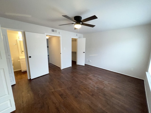 unfurnished bedroom featuring ensuite bathroom, a walk in closet, ceiling fan, dark hardwood / wood-style flooring, and a closet