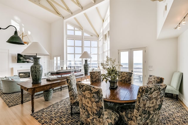 dining room with beam ceiling, french doors, rail lighting, high vaulted ceiling, and light hardwood / wood-style floors