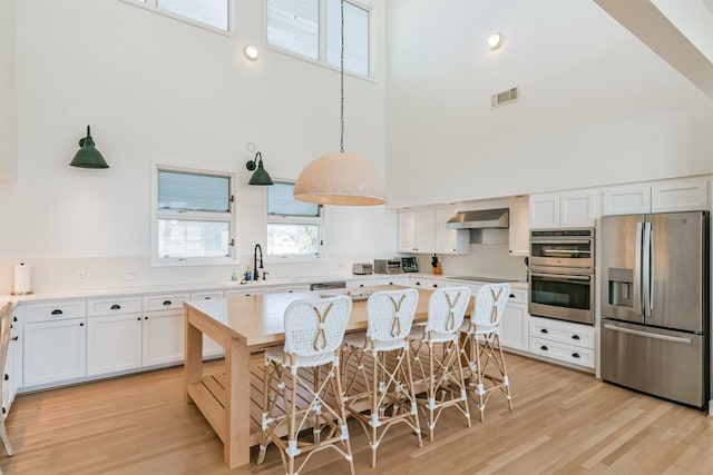 kitchen with a kitchen breakfast bar, a towering ceiling, stainless steel appliances, exhaust hood, and white cabinets