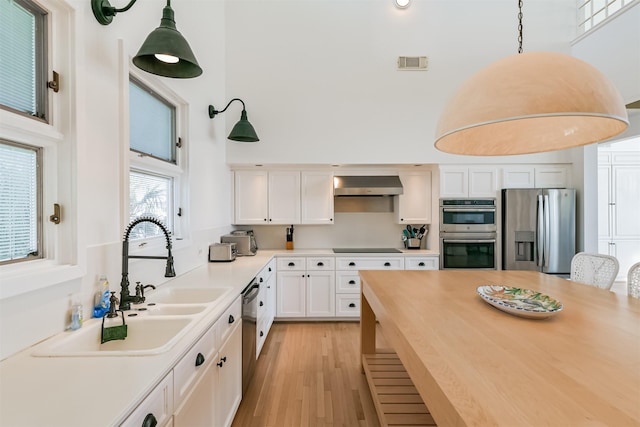 kitchen featuring white cabinetry, extractor fan, hanging light fixtures, and appliances with stainless steel finishes