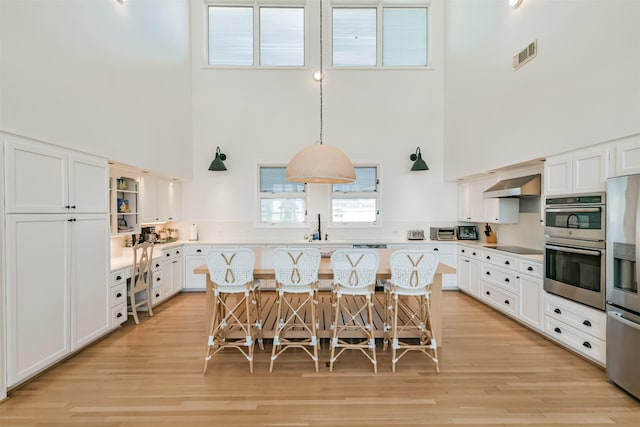 kitchen with pendant lighting, a breakfast bar, white cabinets, a towering ceiling, and a kitchen island