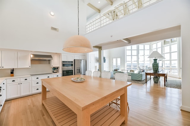 kitchen featuring pendant lighting, ventilation hood, a towering ceiling, white cabinetry, and stainless steel appliances