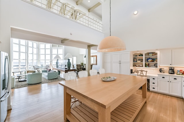 kitchen with light wood-type flooring, a towering ceiling, pendant lighting, beam ceiling, and white cabinetry