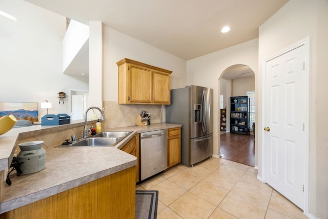 kitchen with decorative backsplash, kitchen peninsula, stainless steel appliances, sink, and light tile patterned flooring