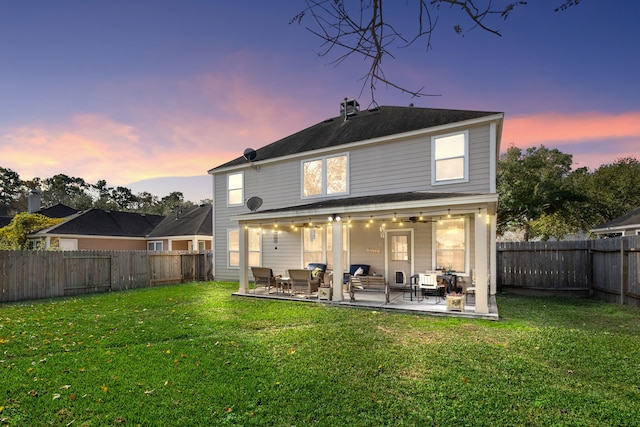 back house at dusk featuring a yard and a patio