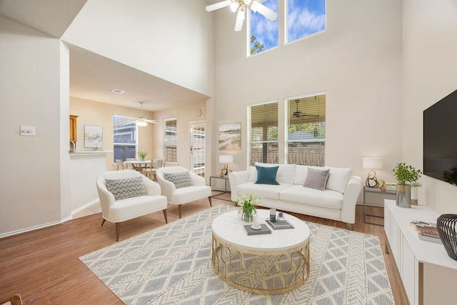 living room featuring ceiling fan, light wood-type flooring, and a high ceiling