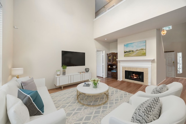 living room with a tiled fireplace, a towering ceiling, and wood-type flooring