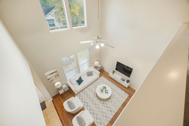 living room with ceiling fan, a healthy amount of sunlight, light wood-type flooring, and a towering ceiling