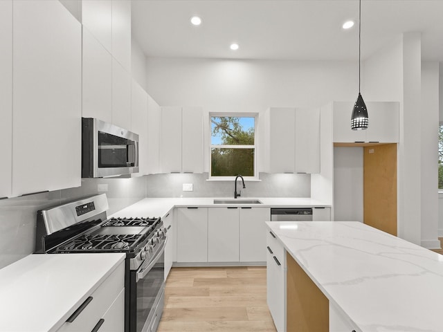 kitchen with light stone countertops, stainless steel appliances, sink, pendant lighting, and white cabinets