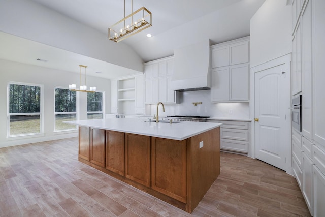 kitchen with an inviting chandelier, premium range hood, white cabinetry, and a center island with sink