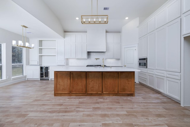 kitchen featuring white cabinets, decorative light fixtures, and a kitchen island with sink