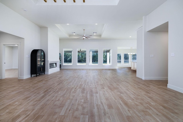 unfurnished living room featuring ceiling fan with notable chandelier, light hardwood / wood-style floors, and a tray ceiling