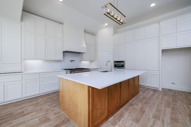 kitchen featuring premium range hood, a kitchen island with sink, white cabinets, and stainless steel appliances