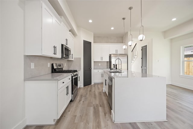 kitchen with hanging light fixtures, white cabinetry, a kitchen island with sink, and appliances with stainless steel finishes