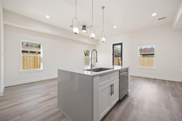 kitchen featuring sink, decorative light fixtures, a center island with sink, white cabinets, and light hardwood / wood-style floors