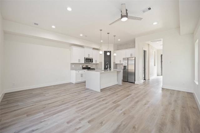 kitchen with stainless steel appliances, an island with sink, pendant lighting, white cabinets, and light wood-type flooring