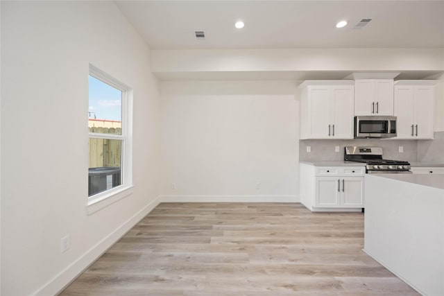 kitchen with decorative backsplash, appliances with stainless steel finishes, light hardwood / wood-style floors, and white cabinetry