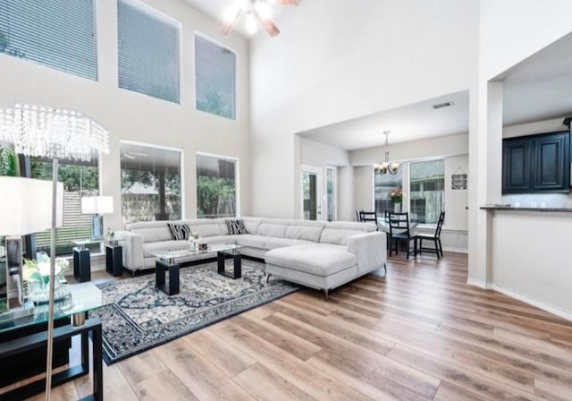 living room with ceiling fan with notable chandelier, light wood-type flooring, and a towering ceiling