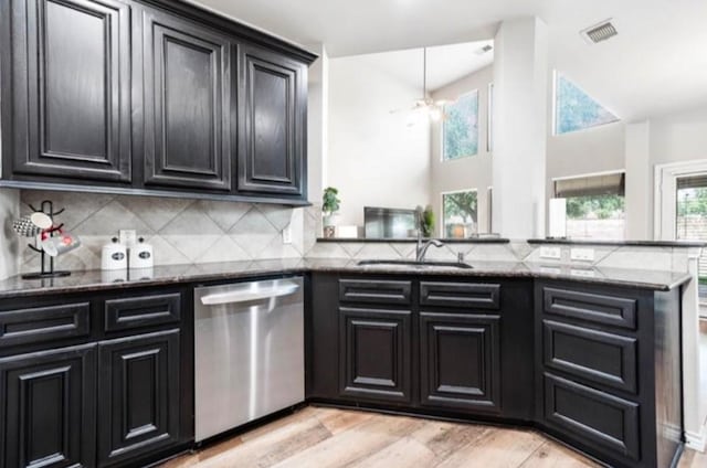 kitchen featuring kitchen peninsula, decorative backsplash, stainless steel dishwasher, dark stone counters, and light hardwood / wood-style floors