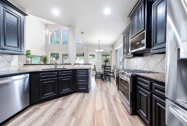 kitchen with light wood-type flooring, tasteful backsplash, stainless steel appliances, pendant lighting, and dark stone countertops