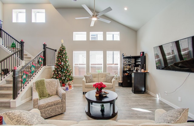 living room featuring ceiling fan, light wood-type flooring, a high ceiling, and indoor bar