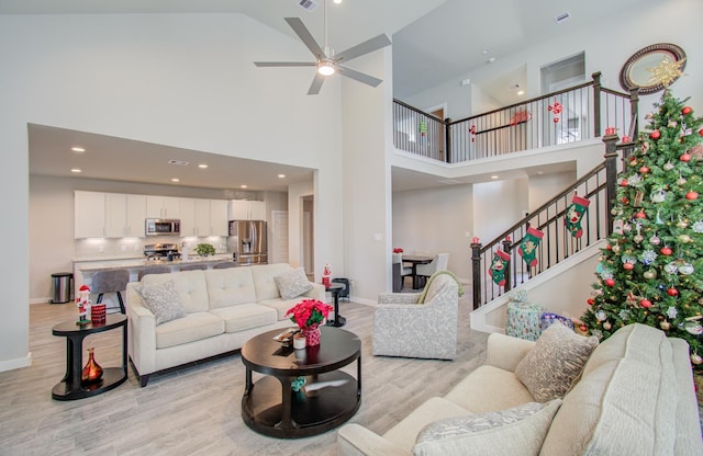 living room with ceiling fan, light hardwood / wood-style floors, and high vaulted ceiling