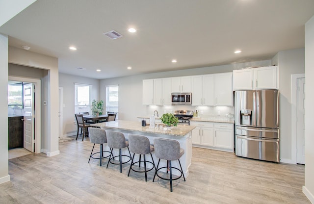 kitchen featuring a breakfast bar, a kitchen island with sink, light stone countertops, white cabinetry, and stainless steel appliances