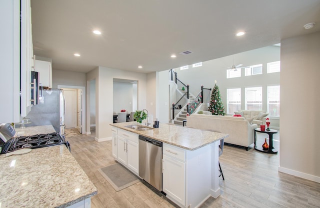 kitchen featuring gas range, dishwasher, sink, a center island with sink, and white cabinets