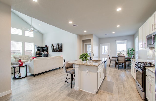 kitchen with a kitchen island with sink, white cabinets, sink, appliances with stainless steel finishes, and light hardwood / wood-style floors