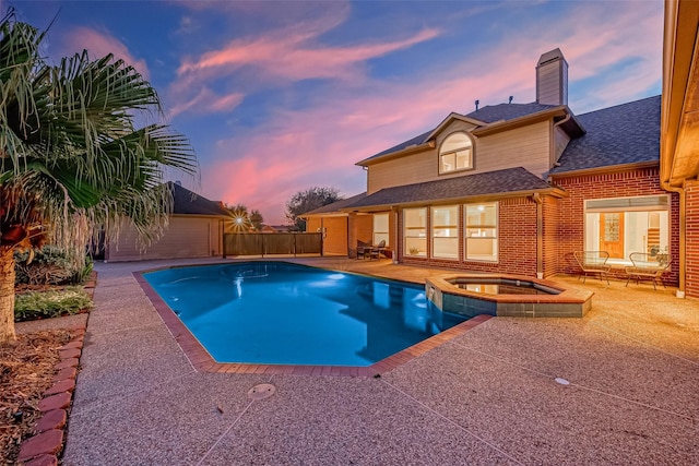 pool at dusk featuring a patio area and an in ground hot tub