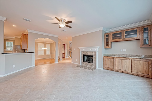 unfurnished living room featuring ceiling fan with notable chandelier, ornamental molding, light tile patterned floors, and a tiled fireplace