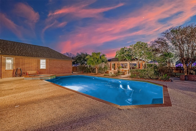 pool at dusk featuring an in ground hot tub and a patio