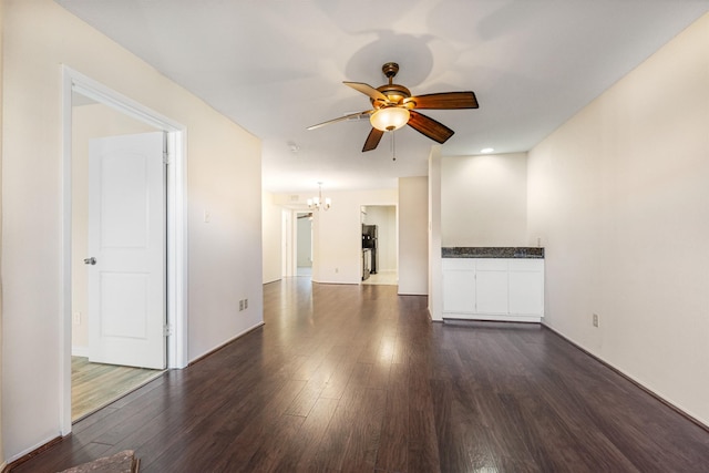 unfurnished living room with ceiling fan with notable chandelier and dark wood-type flooring