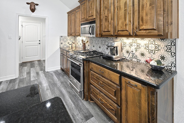 kitchen featuring vaulted ceiling, decorative backsplash, dark hardwood / wood-style floors, dark stone countertops, and appliances with stainless steel finishes