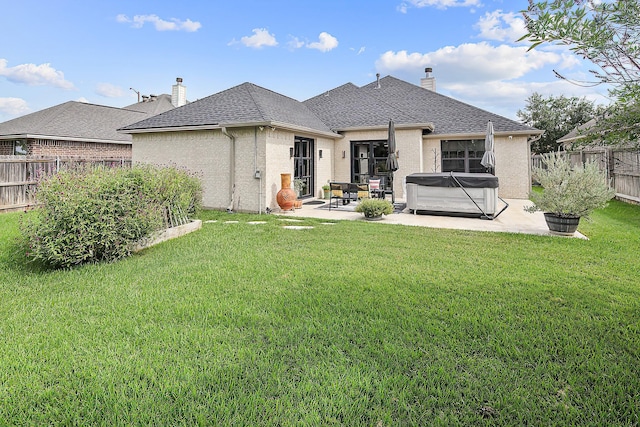 back of property with a lawn, a patio area, and a hot tub