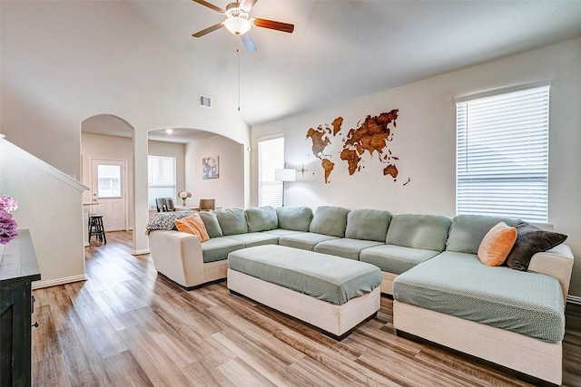 living room with ceiling fan, a towering ceiling, and light hardwood / wood-style flooring