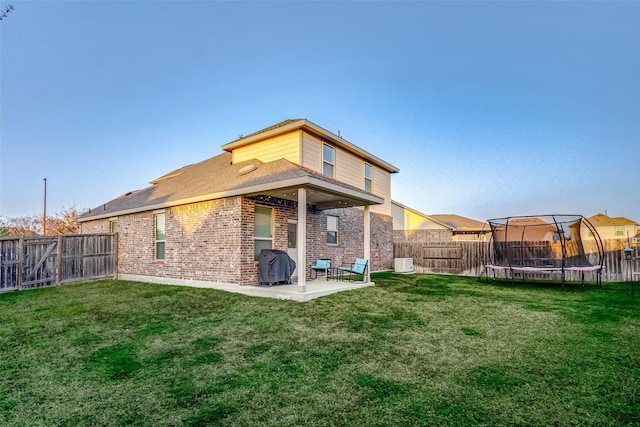 rear view of property with a fenced backyard, a trampoline, a yard, a patio area, and brick siding