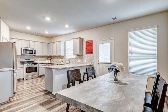 kitchen featuring a breakfast bar, stainless steel appliances, visible vents, backsplash, and a sink