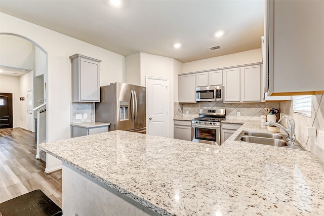 kitchen featuring visible vents, light stone counters, a peninsula, stainless steel appliances, and a sink