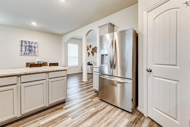 kitchen featuring light stone counters, arched walkways, stainless steel refrigerator with ice dispenser, gray cabinets, and light wood-style flooring