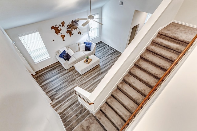 staircase with lofted ceiling, wood finished floors, visible vents, and a ceiling fan